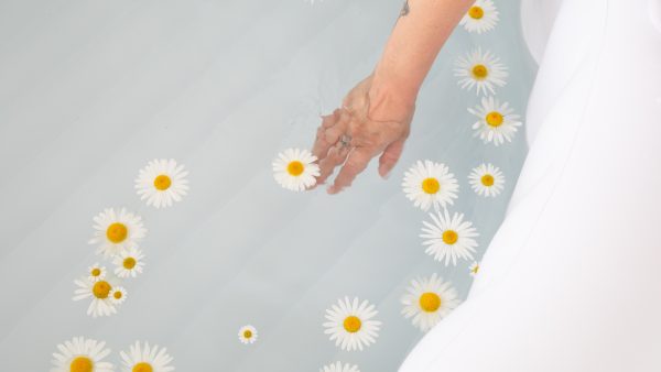 Bloom Birth Pool - filled with water and flowers with a hand in the water